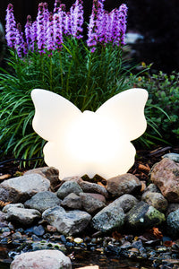 Weiße LED Schmetterlingslampe als dekorative Gartenleuchte zwischen Steinen und Pflanzen