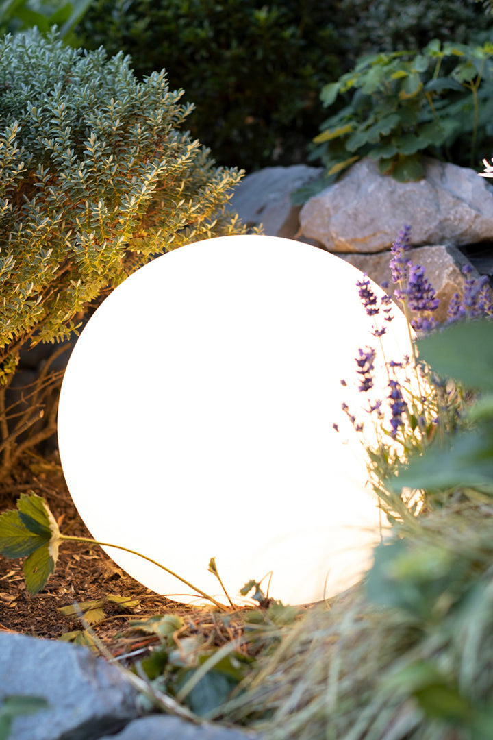 LED Kugelleuchte weiß leuchtend im Blumenbeet zwischen Gartenpflanzen